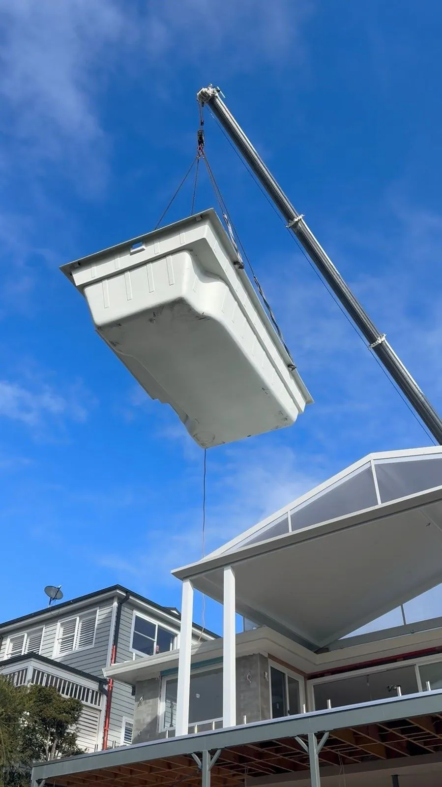 Fibreglass pool shell in the air on the crane, going over the house