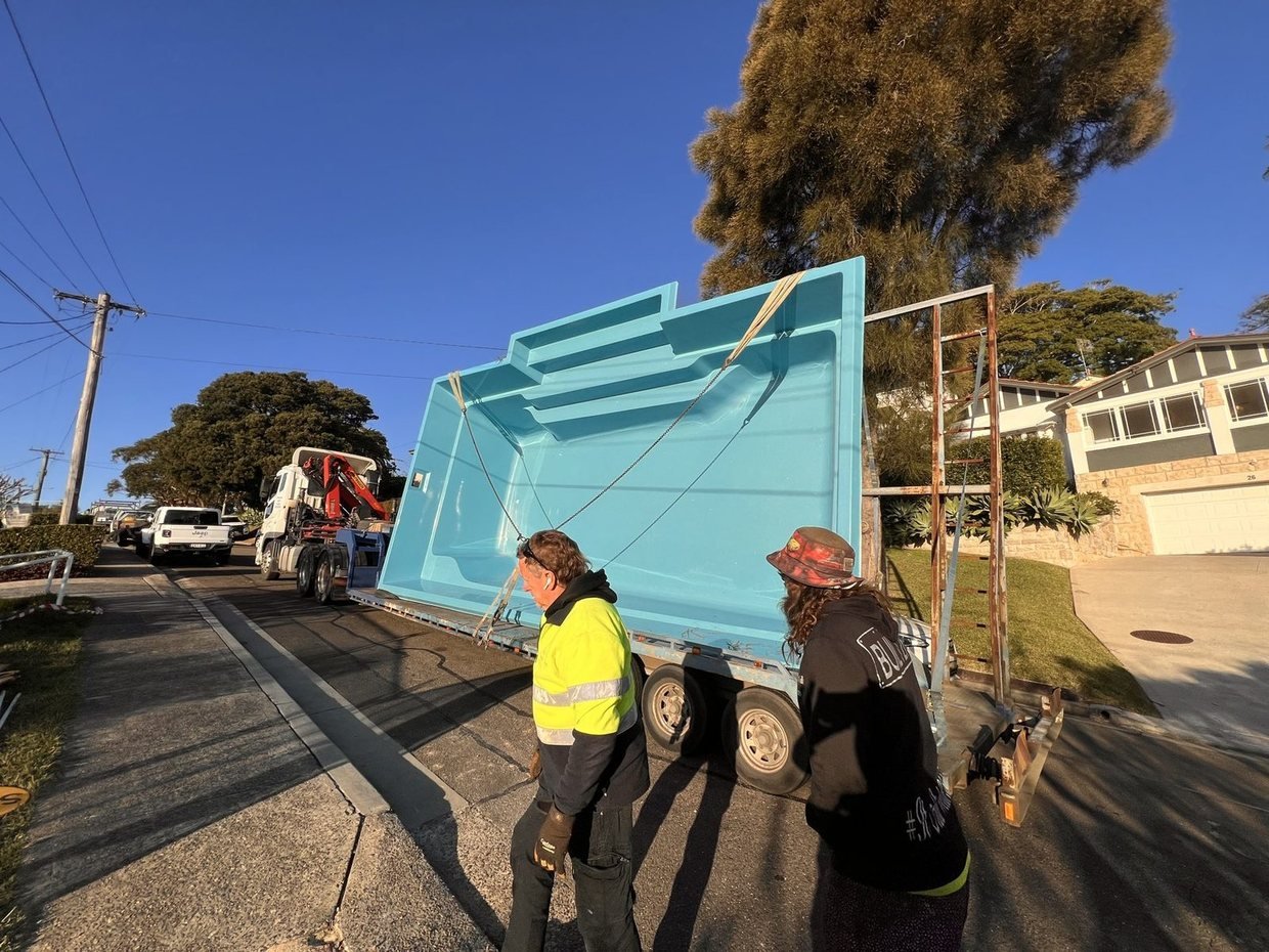 A fibreglass pool shell being lifted from the truck by crane on delivery day